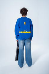 Model in the Haresquare Superhuman Nautical Blue sweatshirt with Yellow print, styled with Haresquare Blue denim jeans and haresquare bag – unisex luxury streetwear from Ireland.